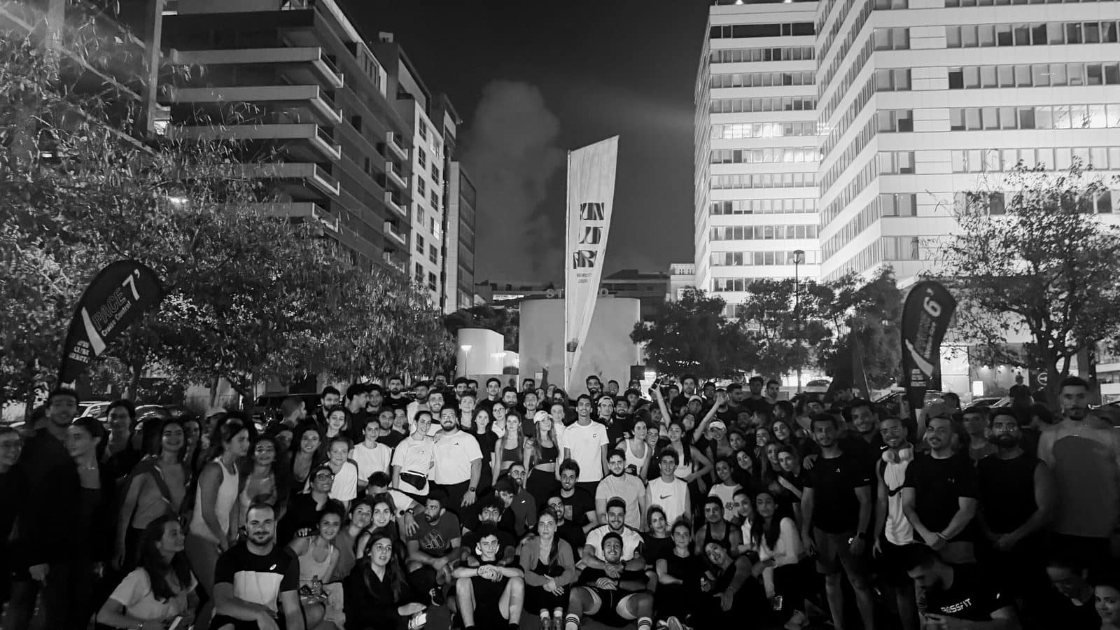 A large Run Club Beirut group gathered under the towers of the city at night, the club flag above them