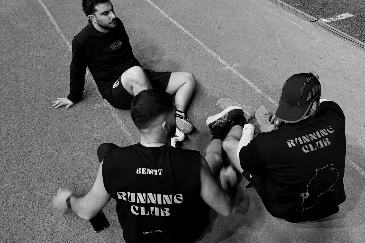 Runners sitting together on a track after a run, talking, club shirts turned to the camera