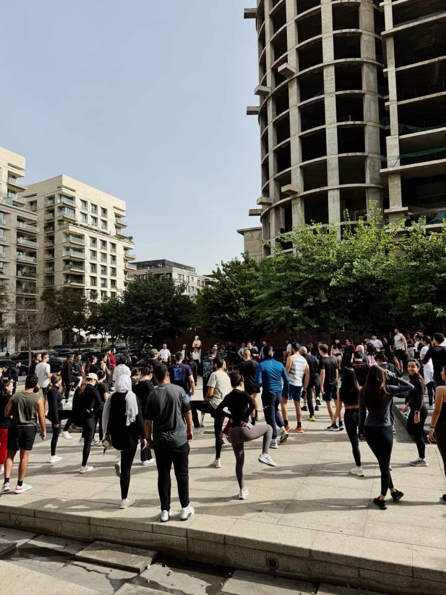 The Run Club Beirut community warming up together in a Beirut plaza, towers behind them